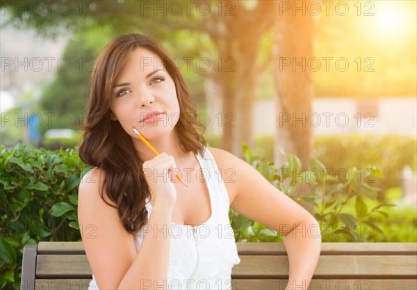 Attractive young adult female student on bench outdoors with books and pencil