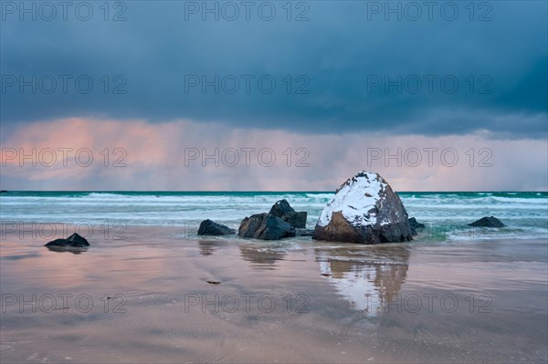 Rocks covered with snow on Norwegian sea beach in fjord in stormy weather with clouds