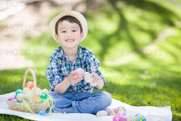 mixed-race chinese and caucasian boy outside wearing rabbit ears playing with easter eggs