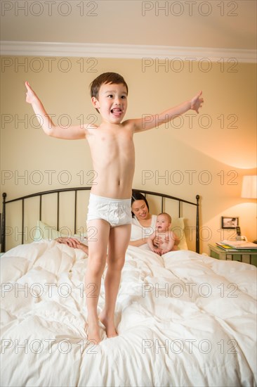 Young mixed-race chinese and caucasian boy jumping in bed with his family