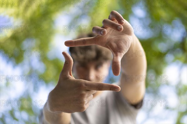 A handsome young man blinks his eyes and looks through a frame made up of hands. Attractive man make frame by fingers