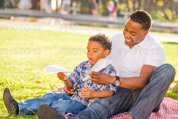 Happy african american father and mixed-race son playing with paper airplanes in the park