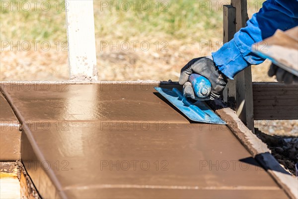 Construction worker using trowel on wet cement forming coping around new pool