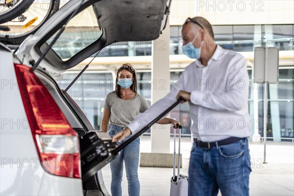 A taxi or Uber driver helping a passenger in a protective mask with her luggage at the airport