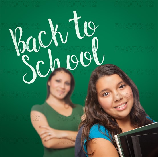 Back to school written on chalk board behind proud hispanic mother and daughter student