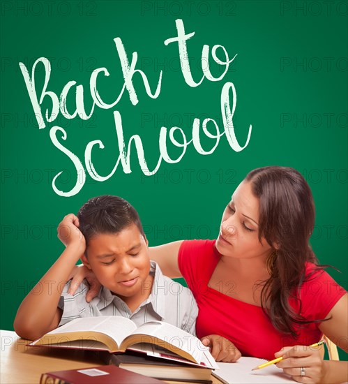 Back to school written on chalk board behind hispanic young boy and famale adult studying