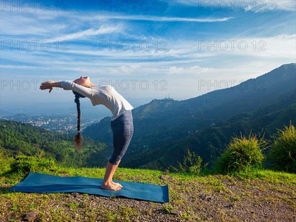 Young sporty fit man doing yoga Sun salutation Surya Namaskar pose Hasta Uttanasana outdoors in mountains