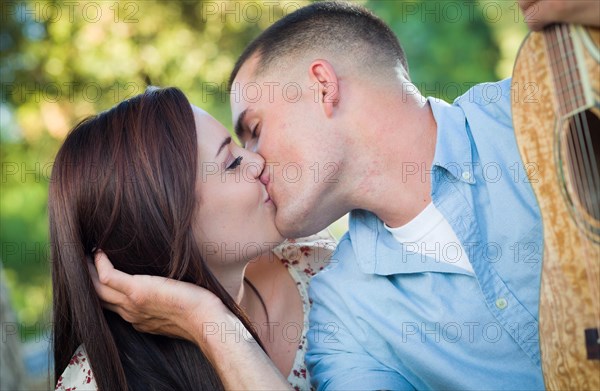 Young couple with guitar kissing in the park