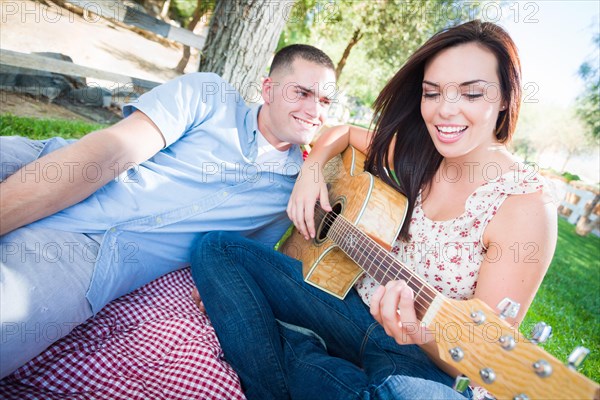 Young adult girl playing guitar with boyfriend in the park