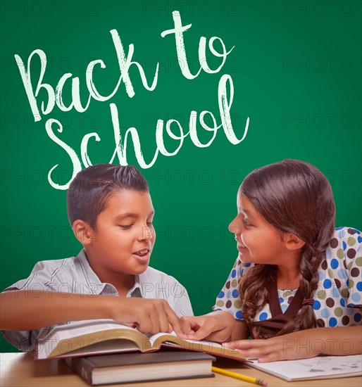 Back to school written on chalk board behind hispanic boy and girl having fun studying together