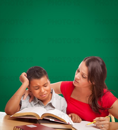 Blank chalk board behind hispanic young boy and famale adult studying