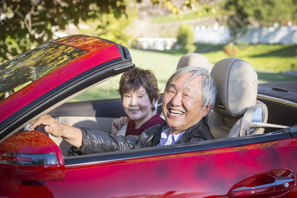 Attractive happy chinese couple enjoying an afternoon drive in their convertible