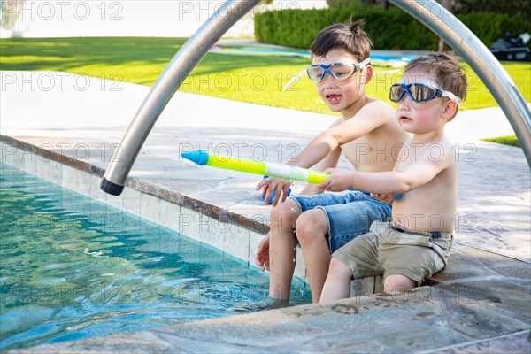 Young mixed-race chinese and caucasian brothers wearing swimming goggles playing at the pool