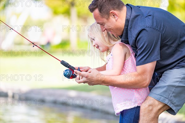 Young caucasian father and daughter having fun fishing at the lake