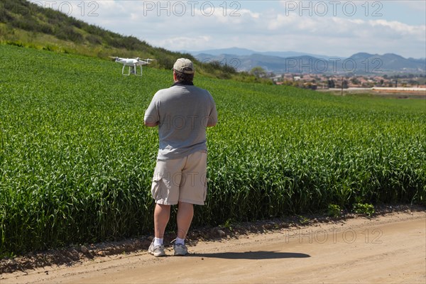 Pilot flying unmanned aircraft drone gathering data over country farmland field