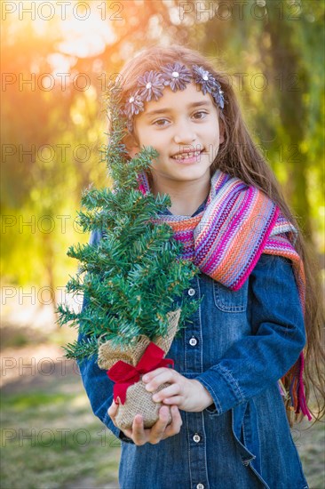 Cute mixed-race young girl holding small christmas tree outdoors