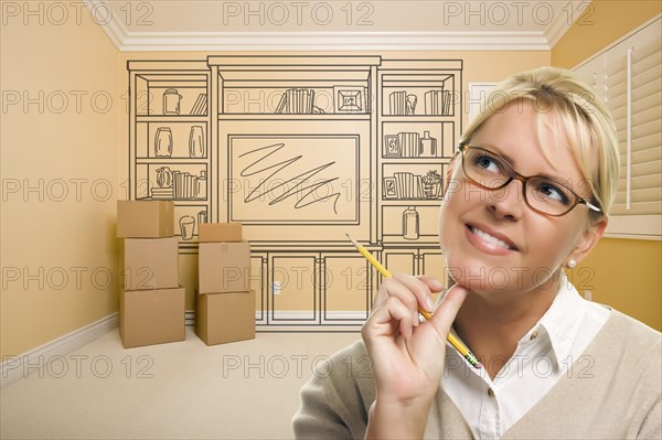 Daydreaming woman holding pencil in empty rom with built in shelf design drawing on wall