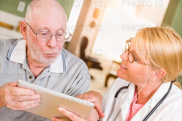 Female doctor or nurse showing senior man touch pad computer at home