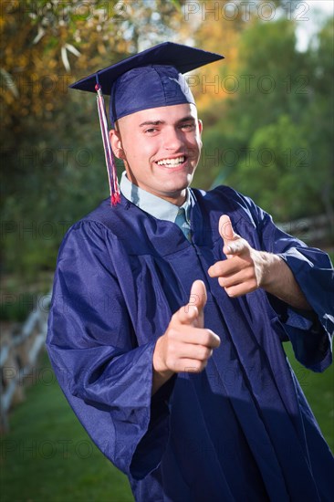 Happy handsome male graduate in cap and gown outside