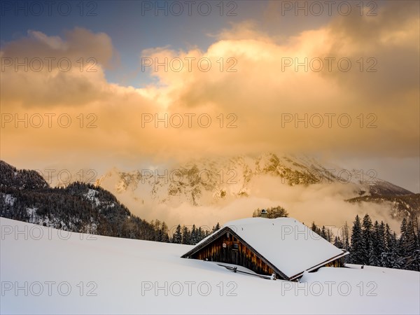 Snow-covered Priesbergalm in front of cloud-covered Watzmann