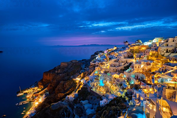 Famous greek iconic selfie spot tourist destination Oia village with traditional white houses and windmills in Santorini island in the evening blue hour