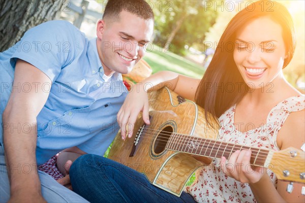 Happy mixed-race couple at the park playing guitar and singing songs