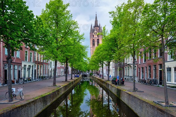 Delt canal with old houses bicycles and cars parked along and Oude Kerk Old church tower