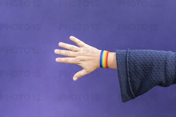 Detail of arm and hand of woman wearing gay wristband on purple background
