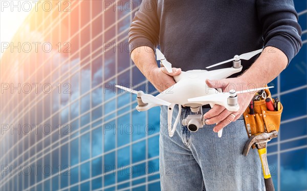 Construction worker and drone pilot with toolbelt holding drone at city high-rise building