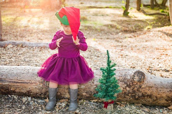 Cute mixed-race young baby girl having fun with christmas hat and tree outdoors