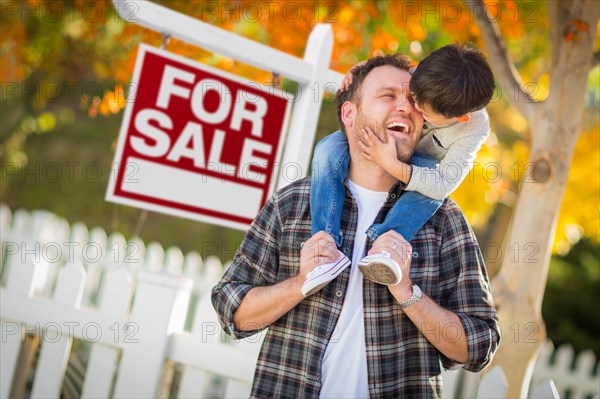 Young mixed-race chinese and caucasian father and son in front of for sale real estate sign and fall yard