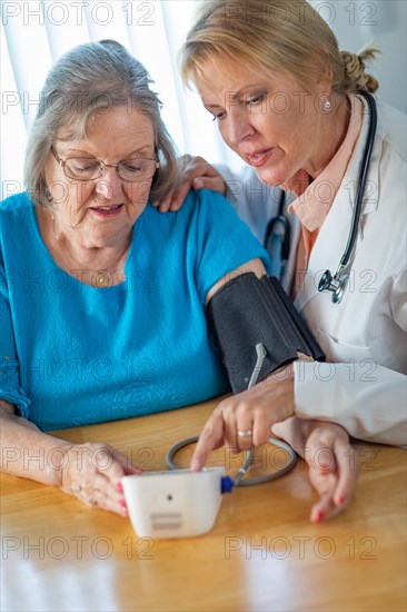 Senior adult woman learning from female doctor to use blood pressure machine