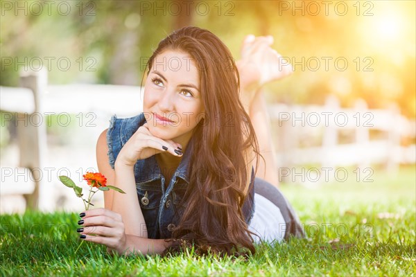 Attractive mixed-race girl daydreaming laying in grass outdoors with flower