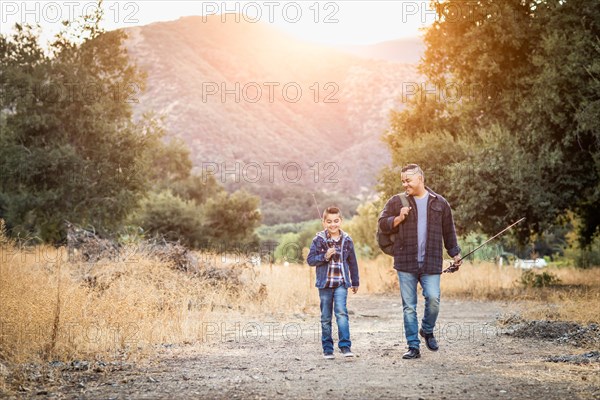 mixed-race father and son outdoors walking with fishing poles