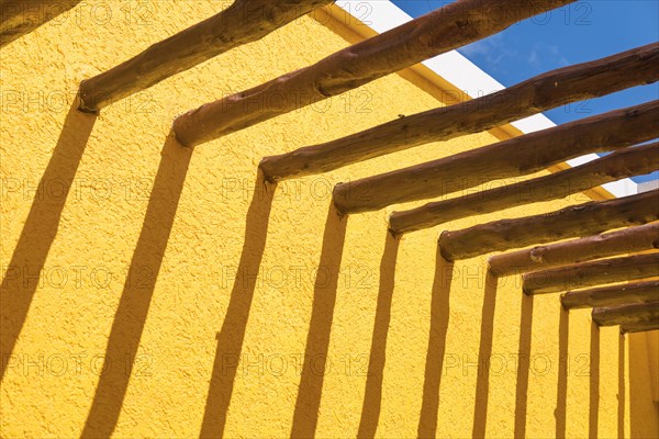 Abstract wooden post beams and bright yellow wall against blue sky