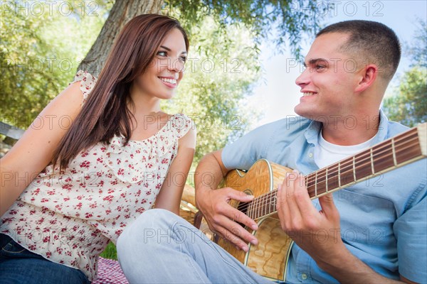 Young adult man playing guitar for his girlfriend in the park