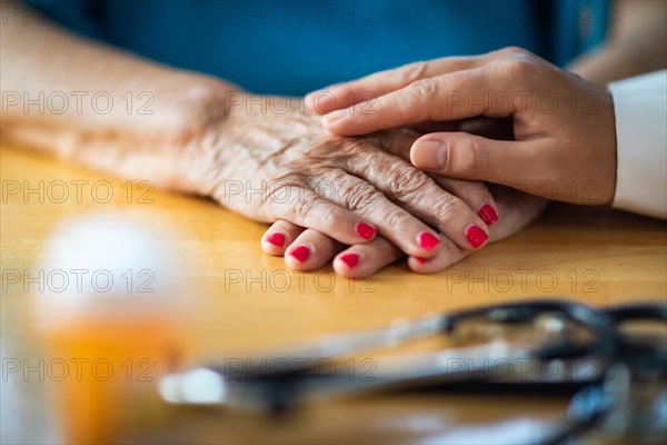 Younger female hands touching senior adult woman hands near stethoscope and medicine bottle