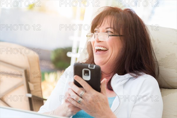 Attractive middle aged woman laughing while using her smart phone on the patio