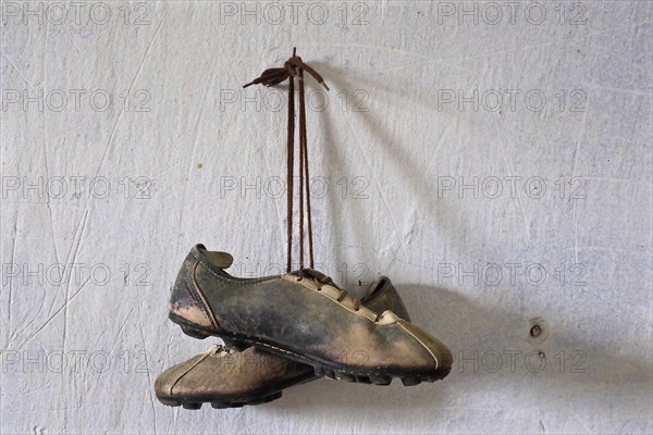 Hanging old leather football boots on nail in front of white wall