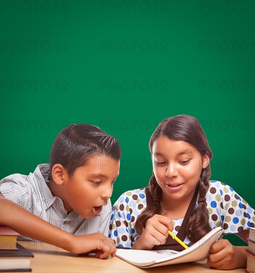 Blank chalk board behind hispanic boy and girl having fun studying together