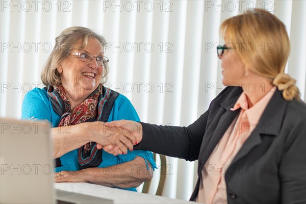 Senoir woman shaking hands with businesswoman near laptop computer