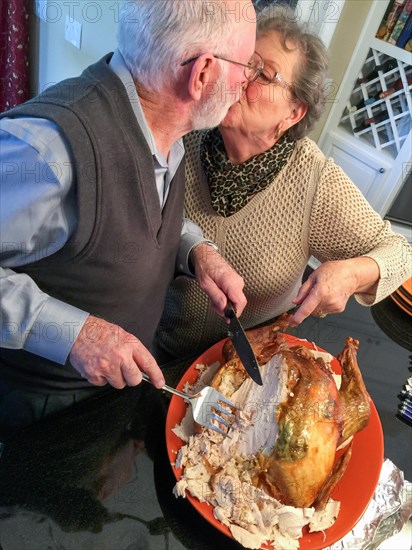 Senior adult couple cutting the holiday Turkey together in the kitchen