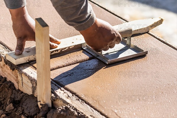 Construction worker using hand groover on wet cement forming coping around new pool