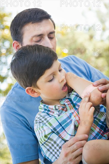 Loving father puts a bandage on the elbow of his young son in the park