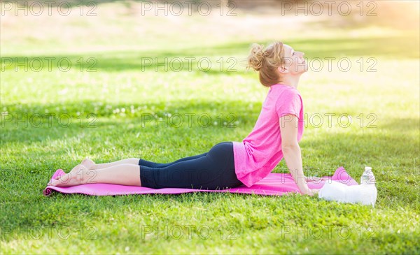 Young fit adult woman outdoors on the grass doing the upward dog yoga pose