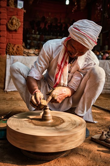 Indian potter at work: throwing the potter's wheel and shaping ceramic vessel and clay ware: pot