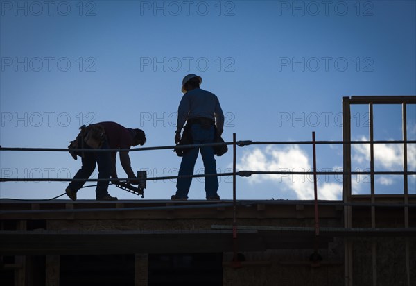 Construction workers silhouette on roof of building