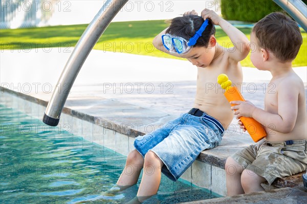 Young mixed-race chinese and caucasian brothers wearing swimming goggles playing at the pool