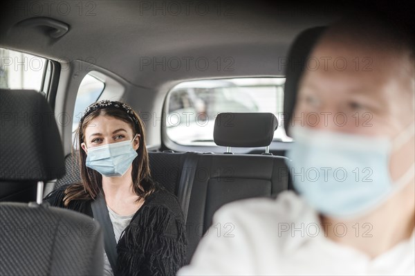 A woman wearing a protective mask sitting on the back seat of a taxi car