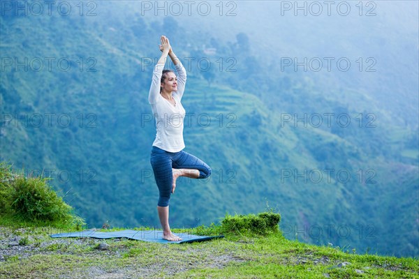 Woman practices balance yoga asana Vrikshasana tree pose in Himalayas mountains outdoors. Himachal Pradesh